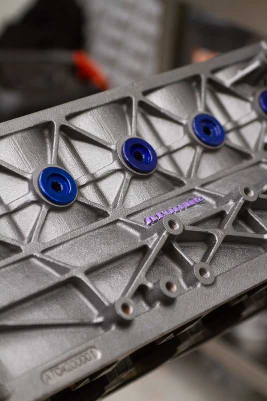 Metal engine block with blue bolts and 'Atomic' branding on a blurred background
