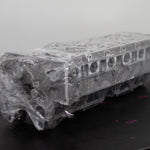 engine cylinder head wrapped in plastic on a black bench with a white background